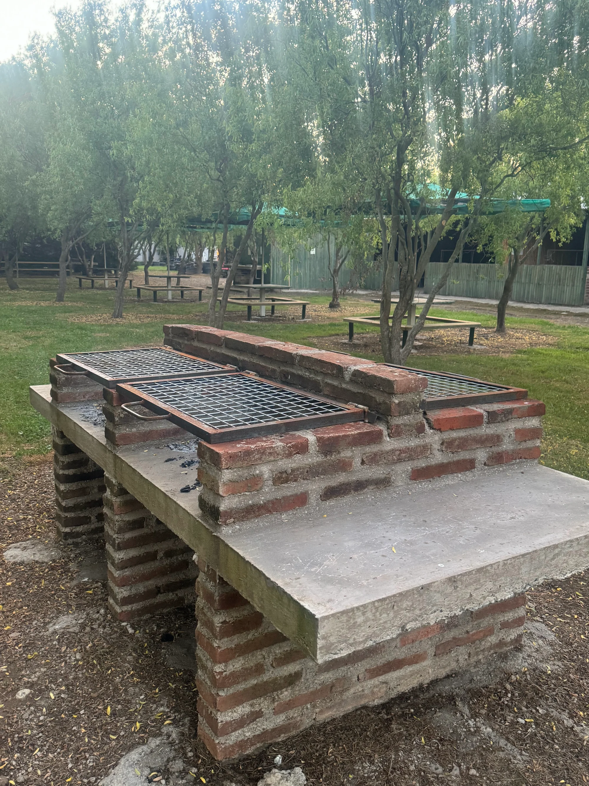 Asadera de ladrillo con parrilla en las áreas verdes entre los sauces