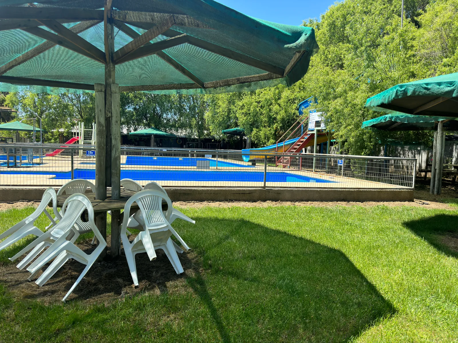 Césped, sillas y sombra junto a las piscinas del parque