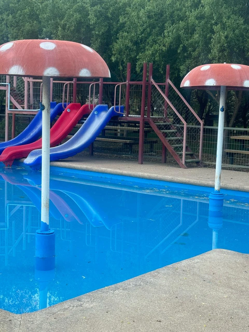 Tres canales de tobogán rojos y azules junto a las fuentes de hongos de la piscina infantil