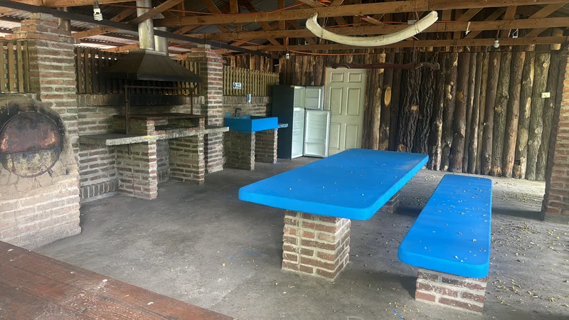 Interior de un quincho con asadera de ladrillo y mesas azules